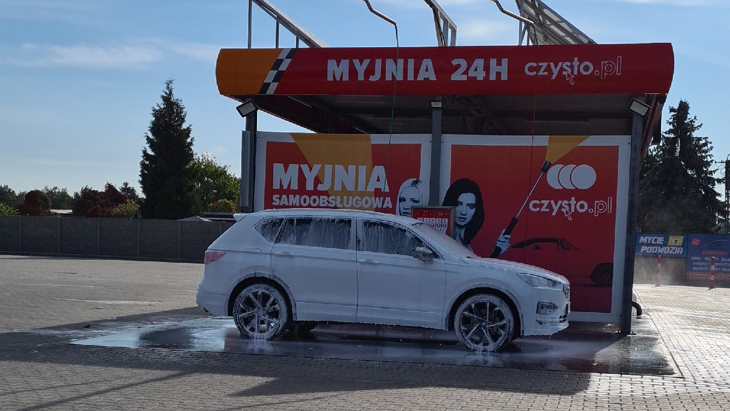 Myjnia samoobsługowa Jedynka w Zduńskiej Woli - białe auto pokryte aktywną pianą pod czerwoną wiatą z napisem MYJNIA 24H.